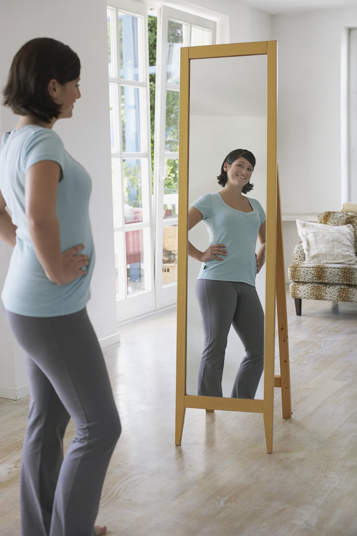 Woman looking at her reflection in a full body mirror with her hands on her hips and smiling