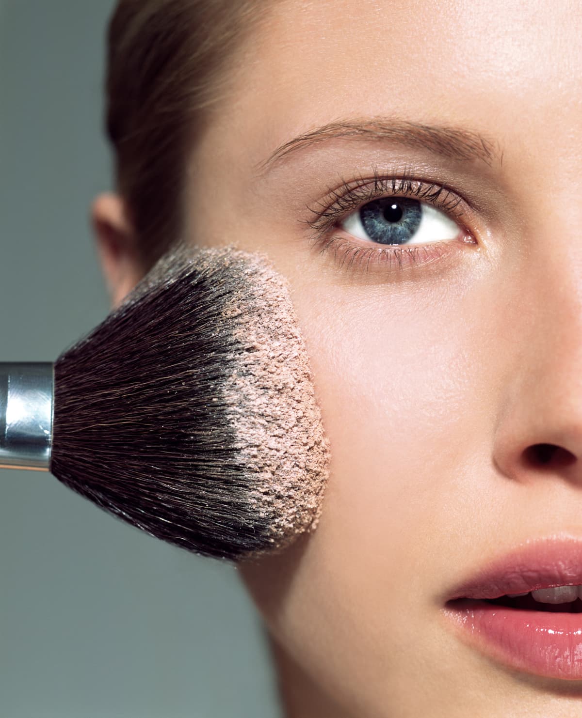Close up of woman applying a face powder with a large makeup brush