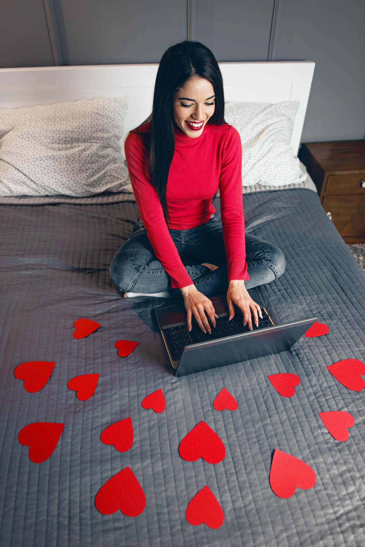 Beautiful young woman surrounded with red hearts, using a laptop