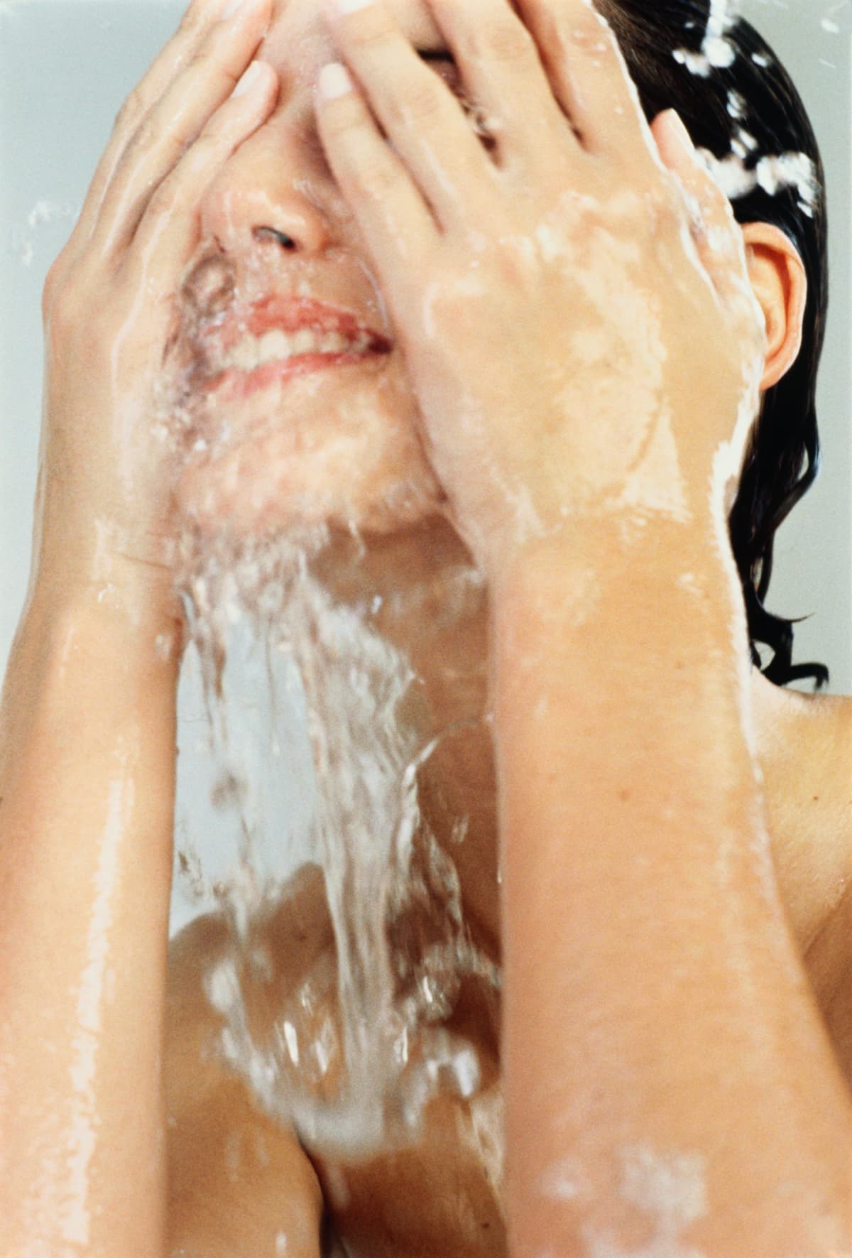 Cropped shot of a beautiful young woman washing her face against a grey background