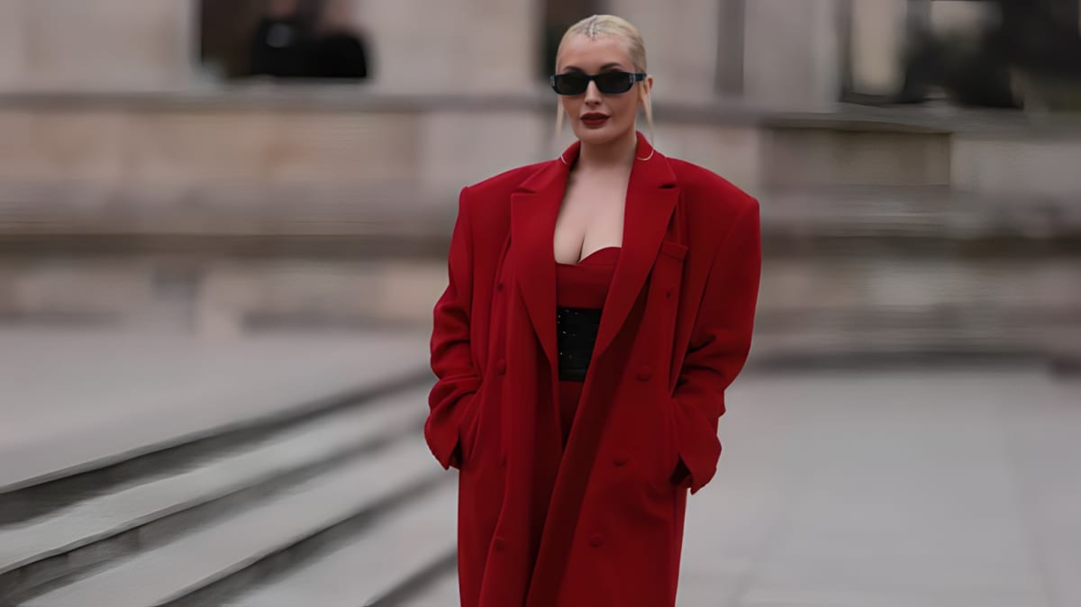 A woman walking in an oversized red coat and black sunglasses