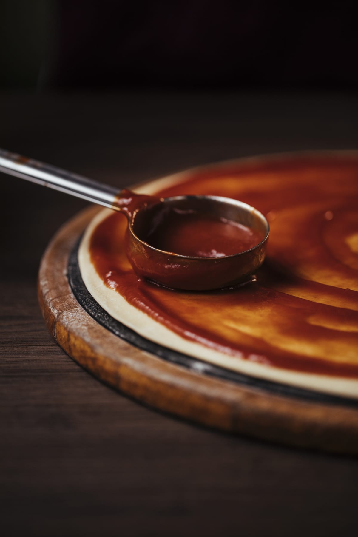 Stock photo showing close-up, elevated view of a rich tomato sauce in a large frying pan being stirred with a wooden spatula as it reduces.  This savoury sauce has had green basil leaf herbs added to it.
