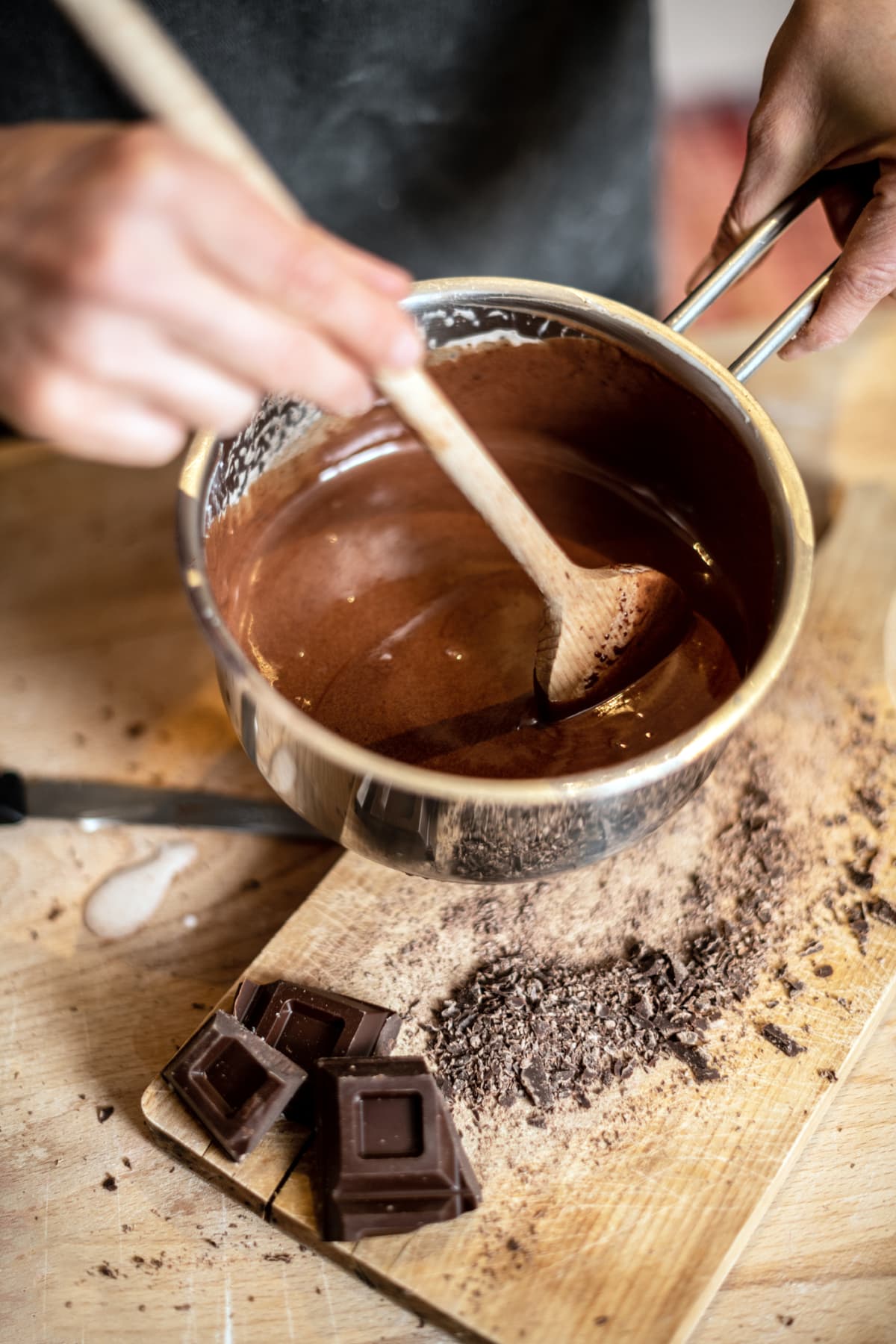 Hand stirring pot of melted chocolate with wooden spoon