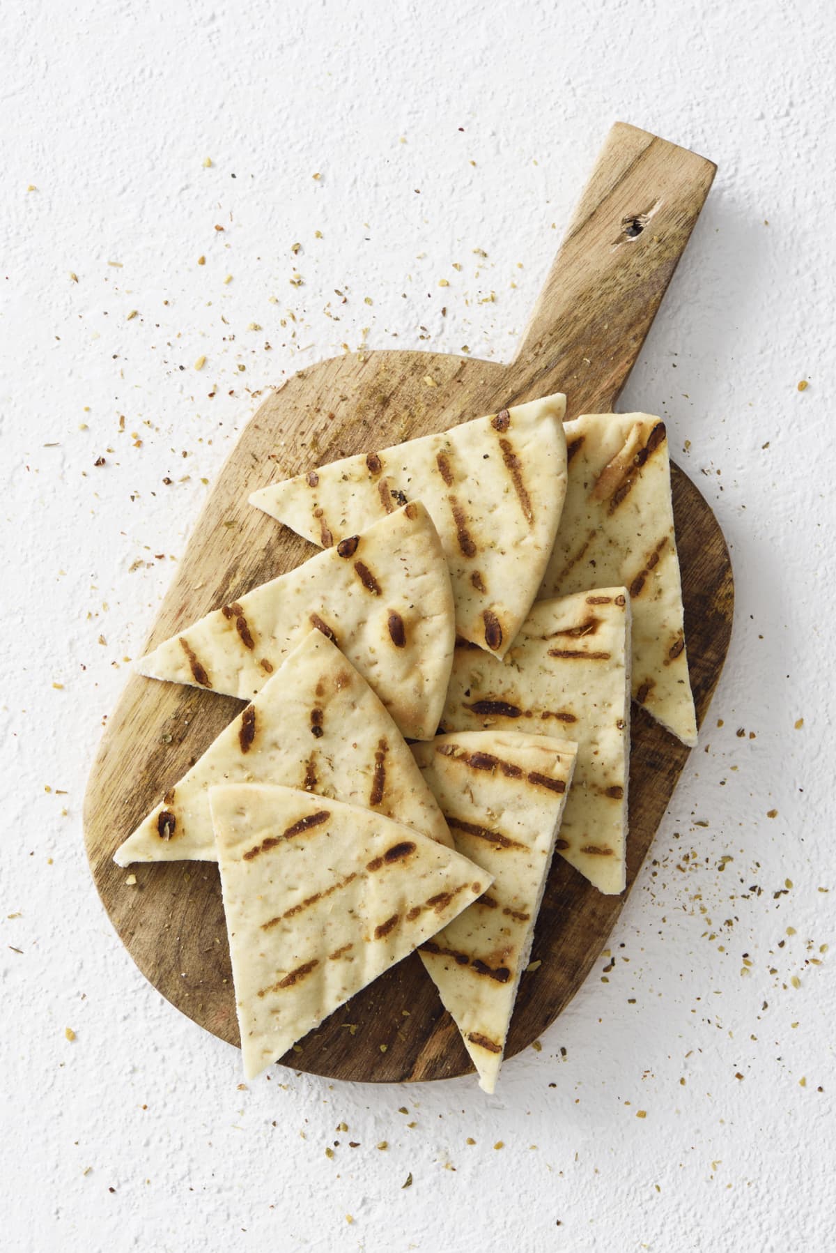 Grilled greek pita bread chips with seasoning on a wooden cutting board