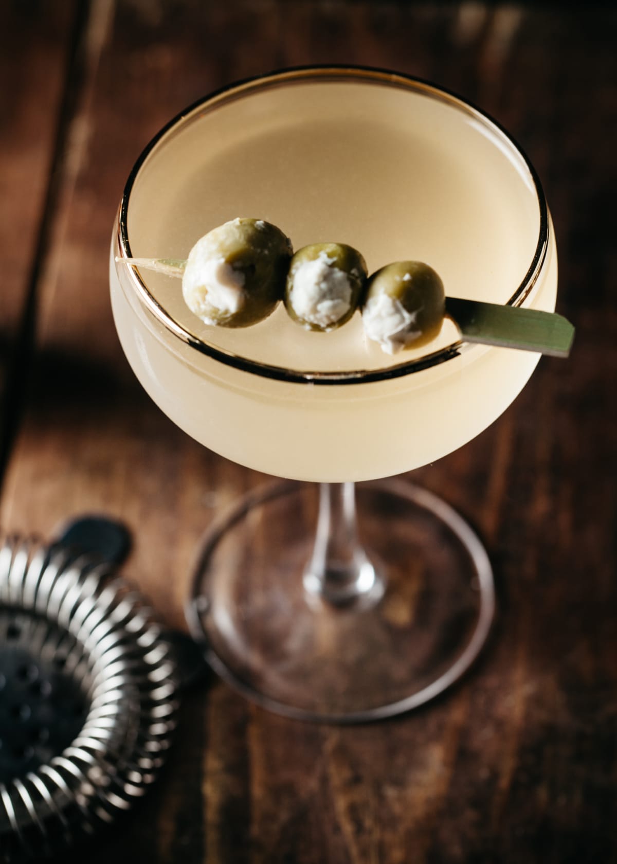 A martini garnished with stuffed olives on wooden surface, vertical