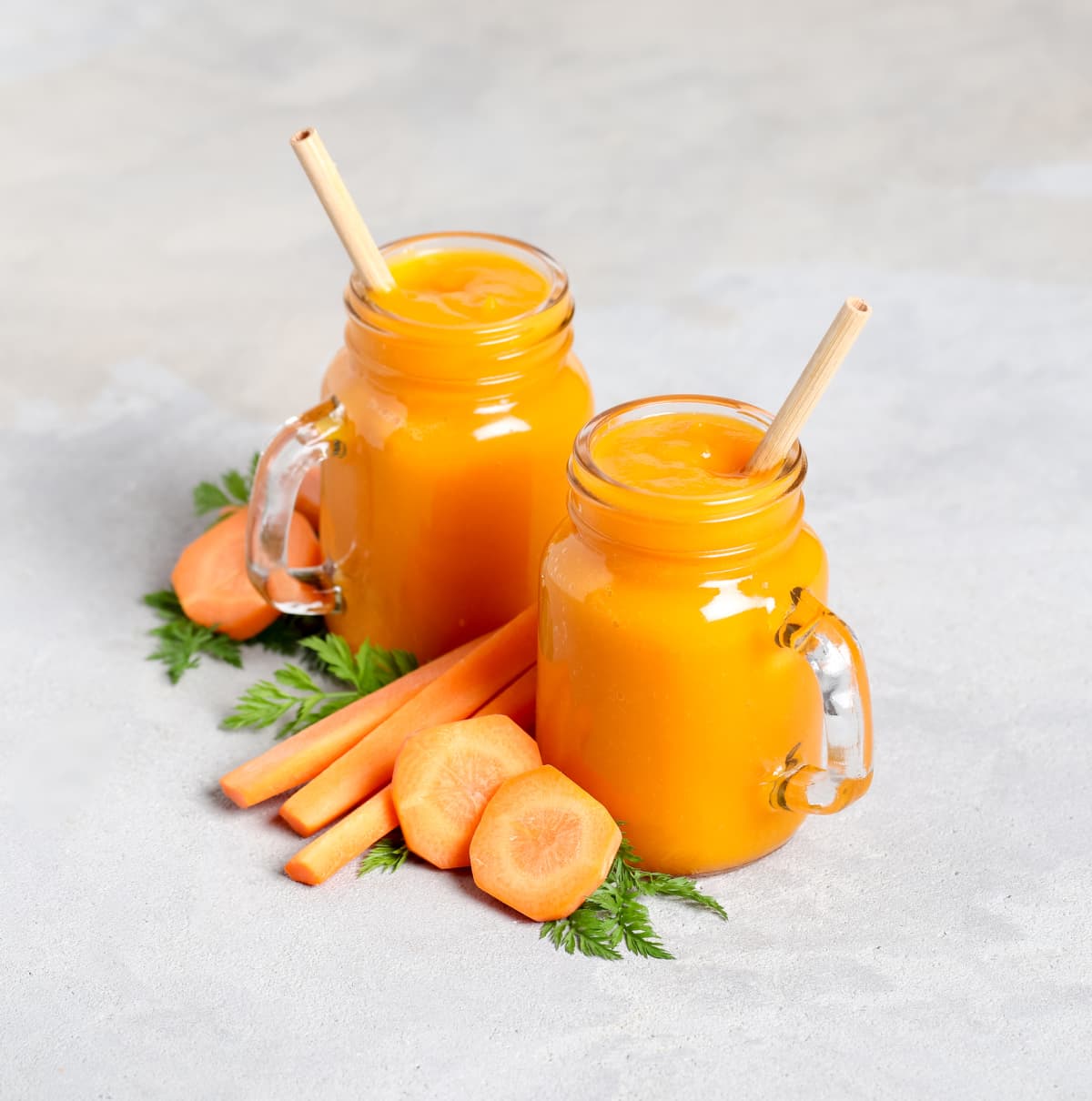 Carrot smoothie in glass jars with a bamboo straws on a light background
