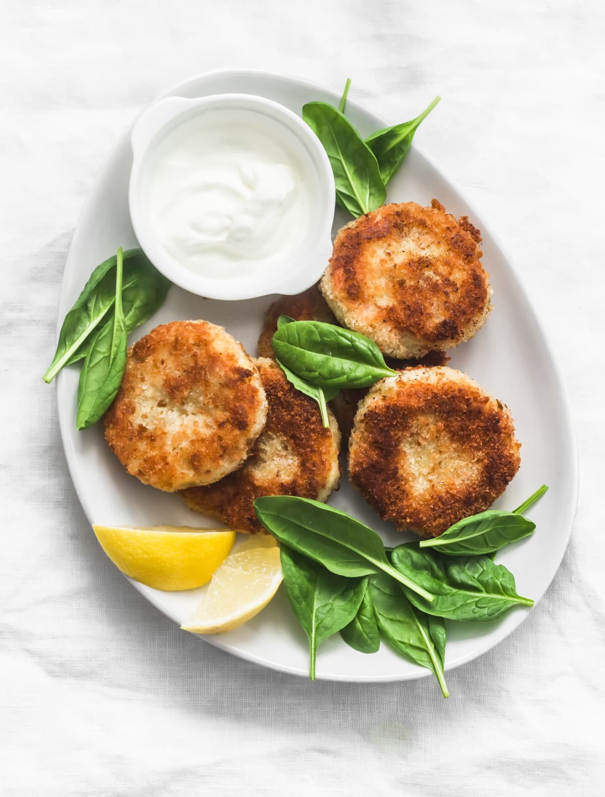 Tuna and potato patties served with spinach and greek yogurt on a light background, top view