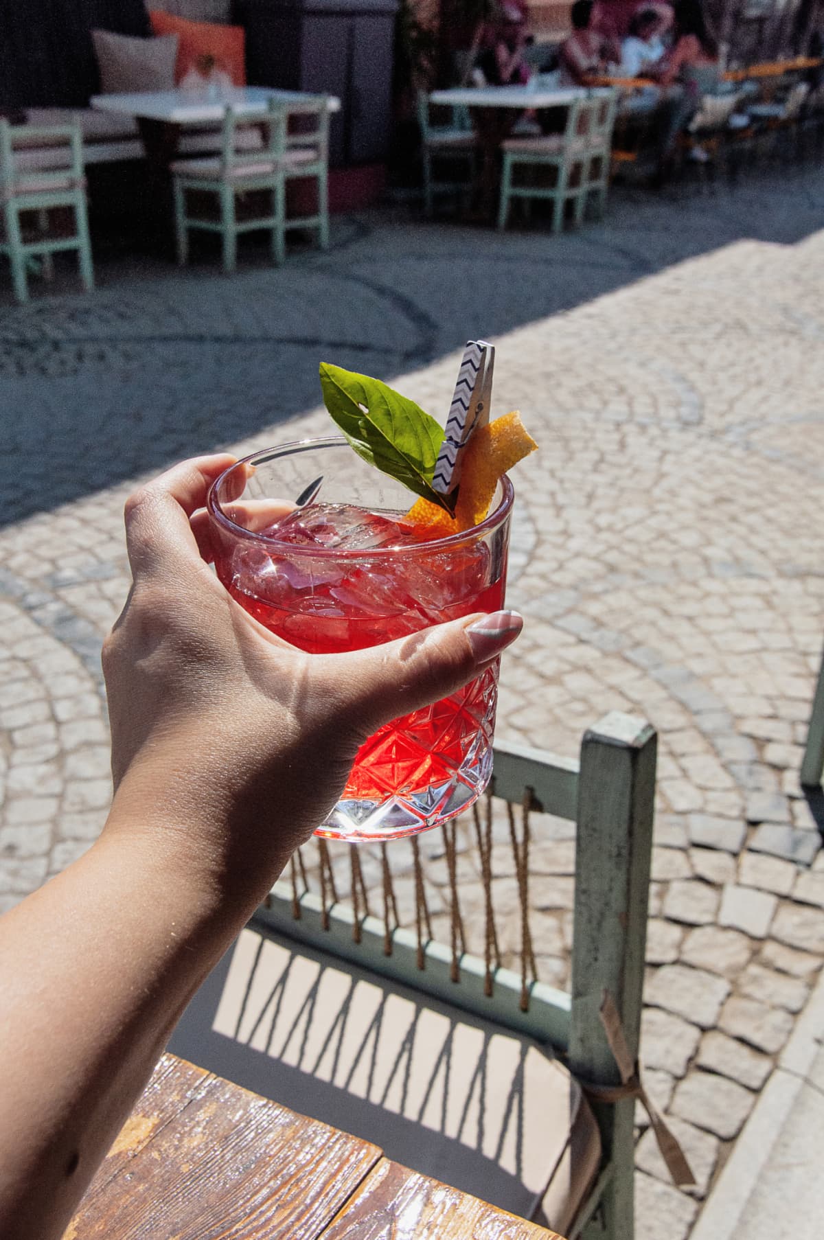 Person holding out a red cocktail in the plaza