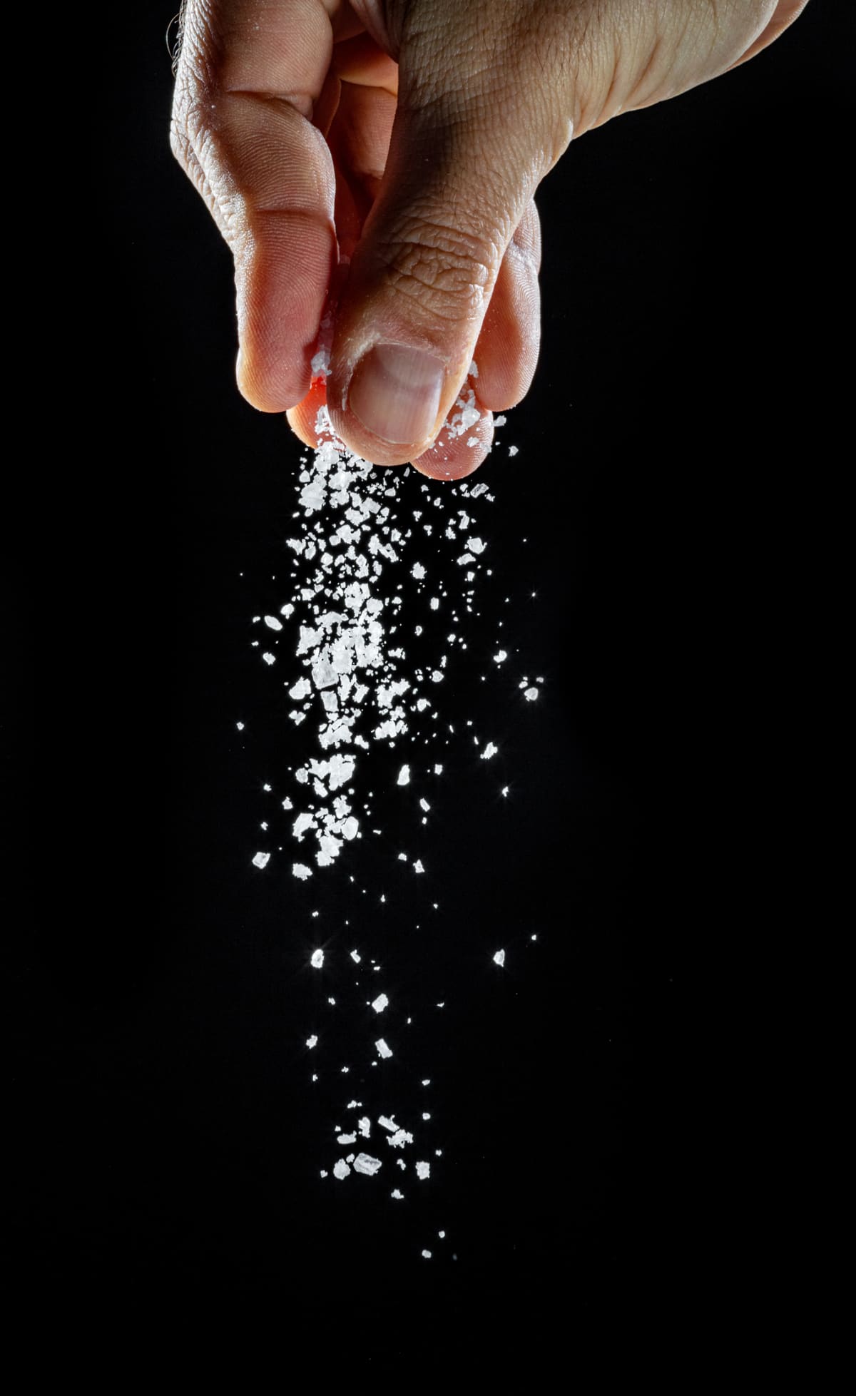 Close up of salt being sprinkled in a wooden spoon on black background.