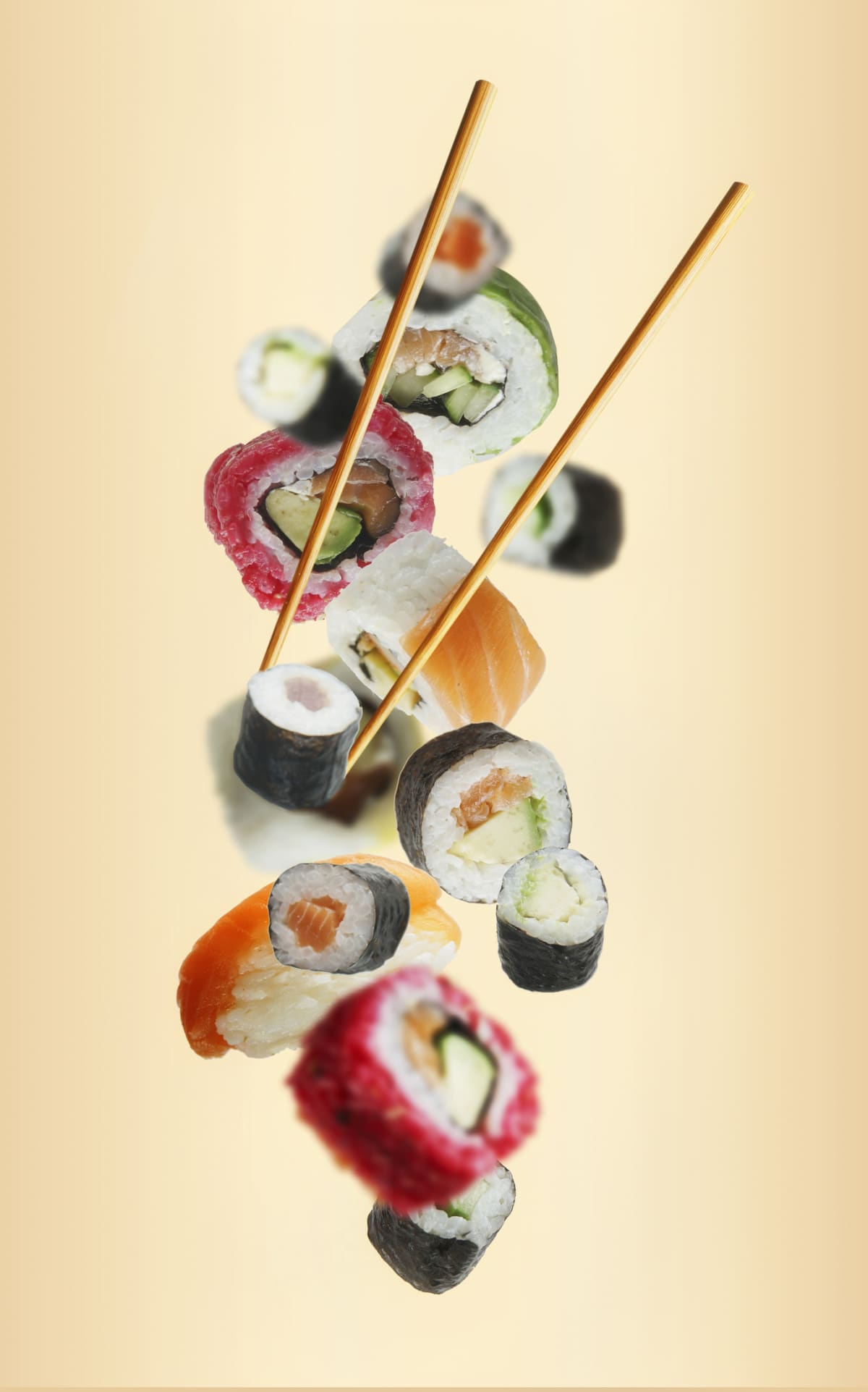 Various flying sushi with chopsticks at light beige background. Maki and nigiri with fresh fish, avocado, cucumber and beetroot. Levitation concept with delicious  food. Front view.
