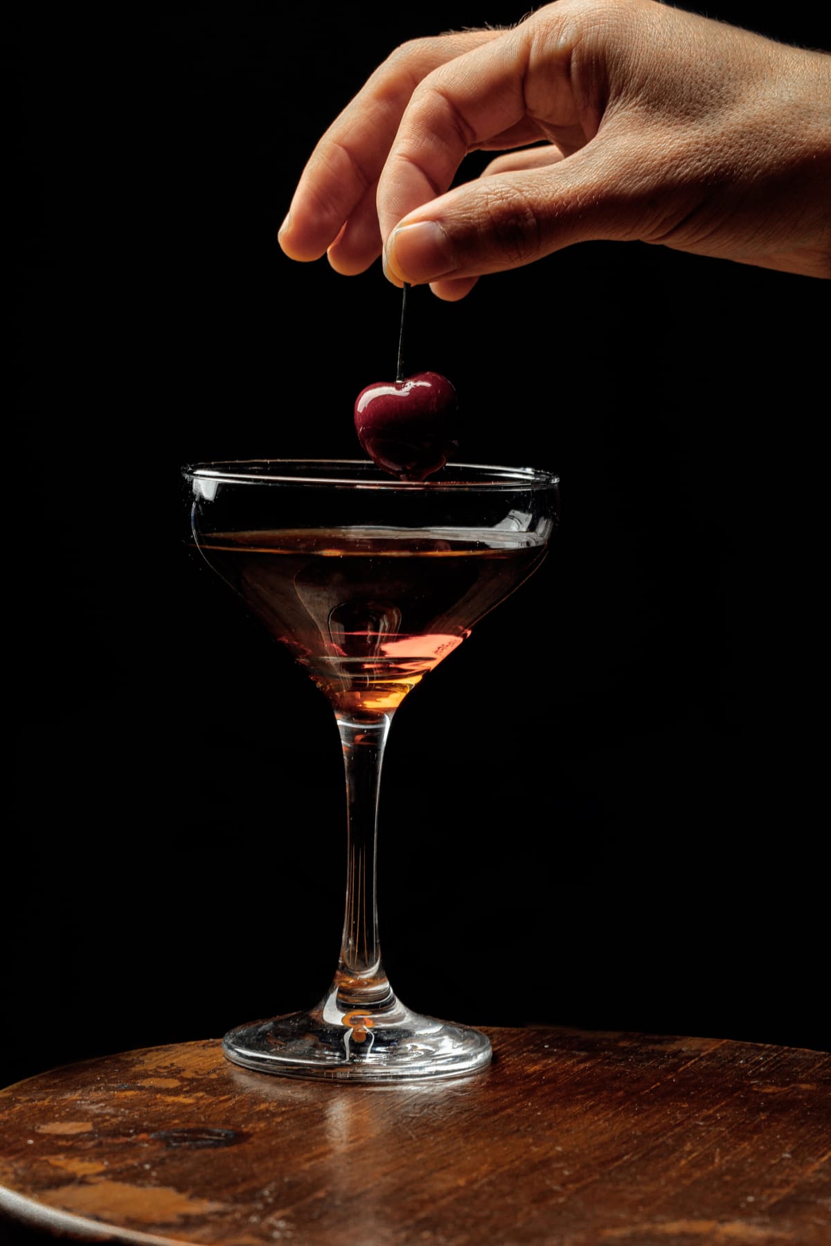 A hand placing a cherry into a Manhattan Cocktail