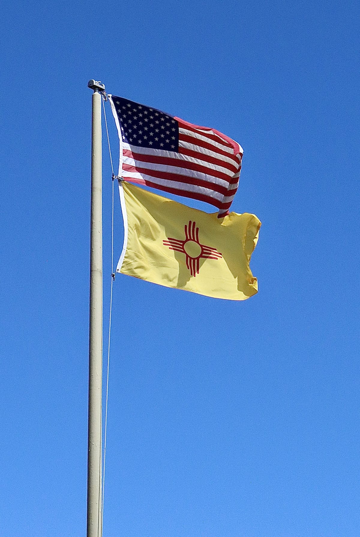 Detail of the flag of the US state of New Mexico on an old piece of paper.  A red sun symbol of the Zia on a field of yellow. The colors honor Isabella of Castile and the conquistadors who explored in her name.