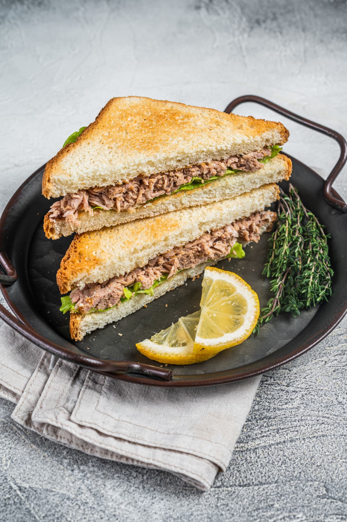 Tuna salad sandwich with lettuce on toasted whole grain bread cut in half on a cutting board