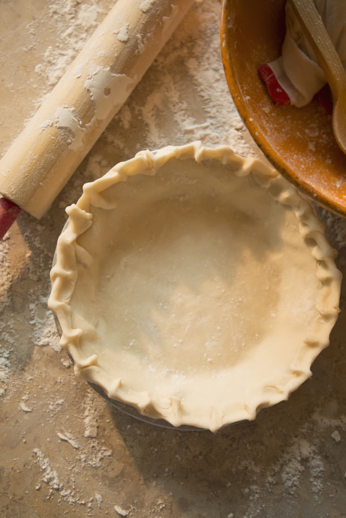 A plain pie crust beside a rolling pin and a bowl.