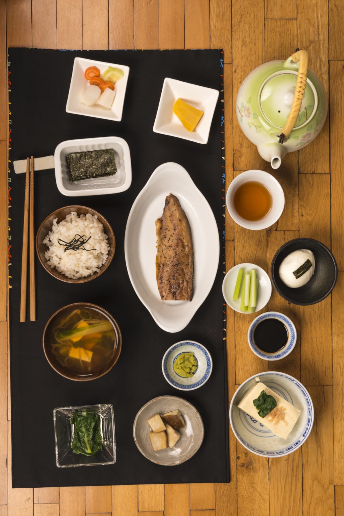 Japanese breakfast with a variety of foods, miso soup, rice, fish, pickel, nori, various vegetables and tea on wooden background.