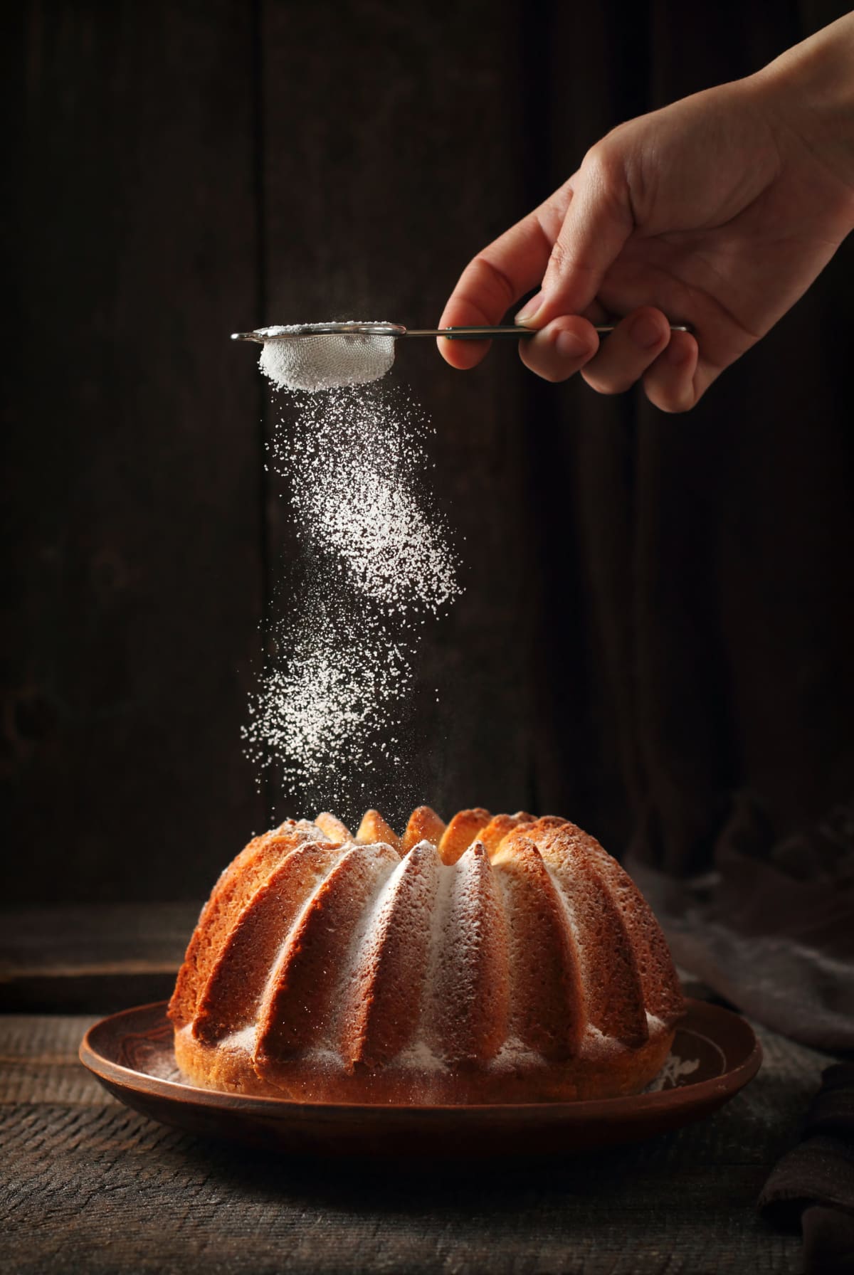 sprinkling of orange cake with powdered sugar, dark wood background, light from one flash and one reflector