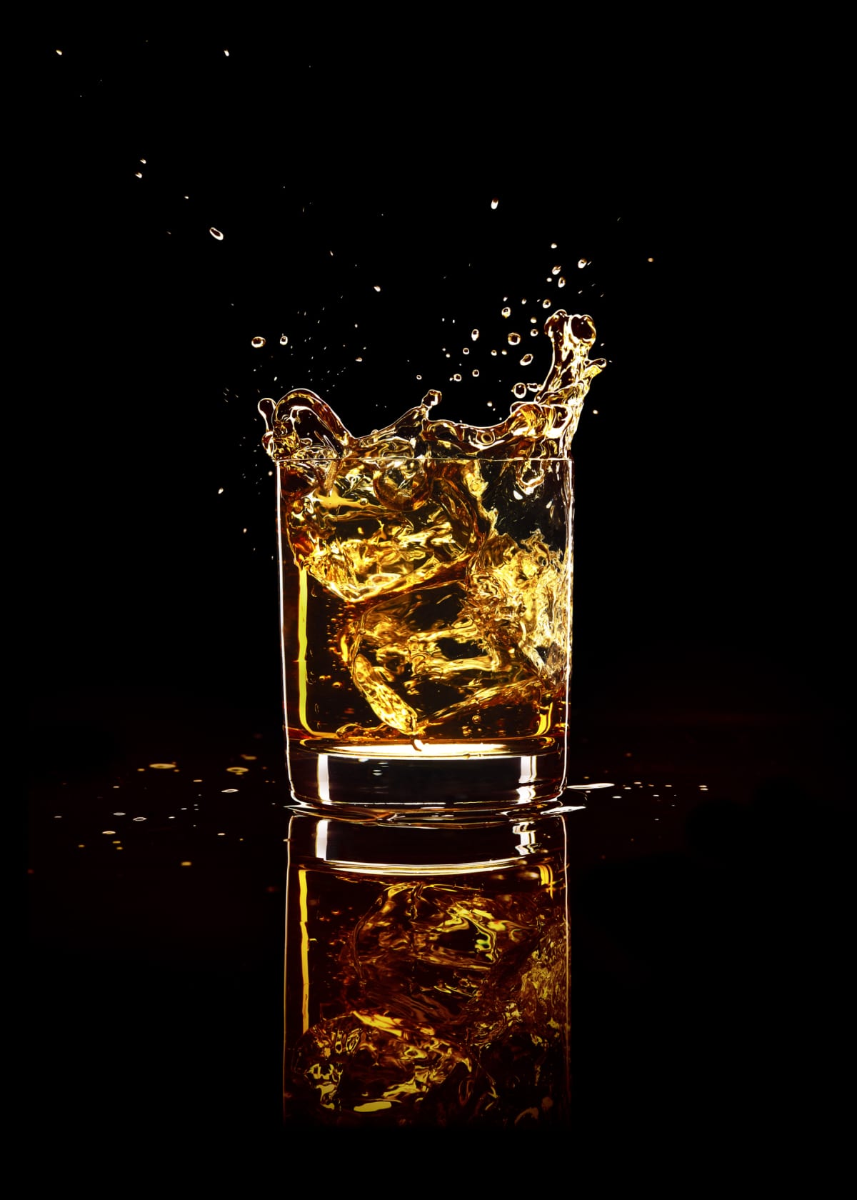 Scotch whiskey splash in glass with natural ice on black background.