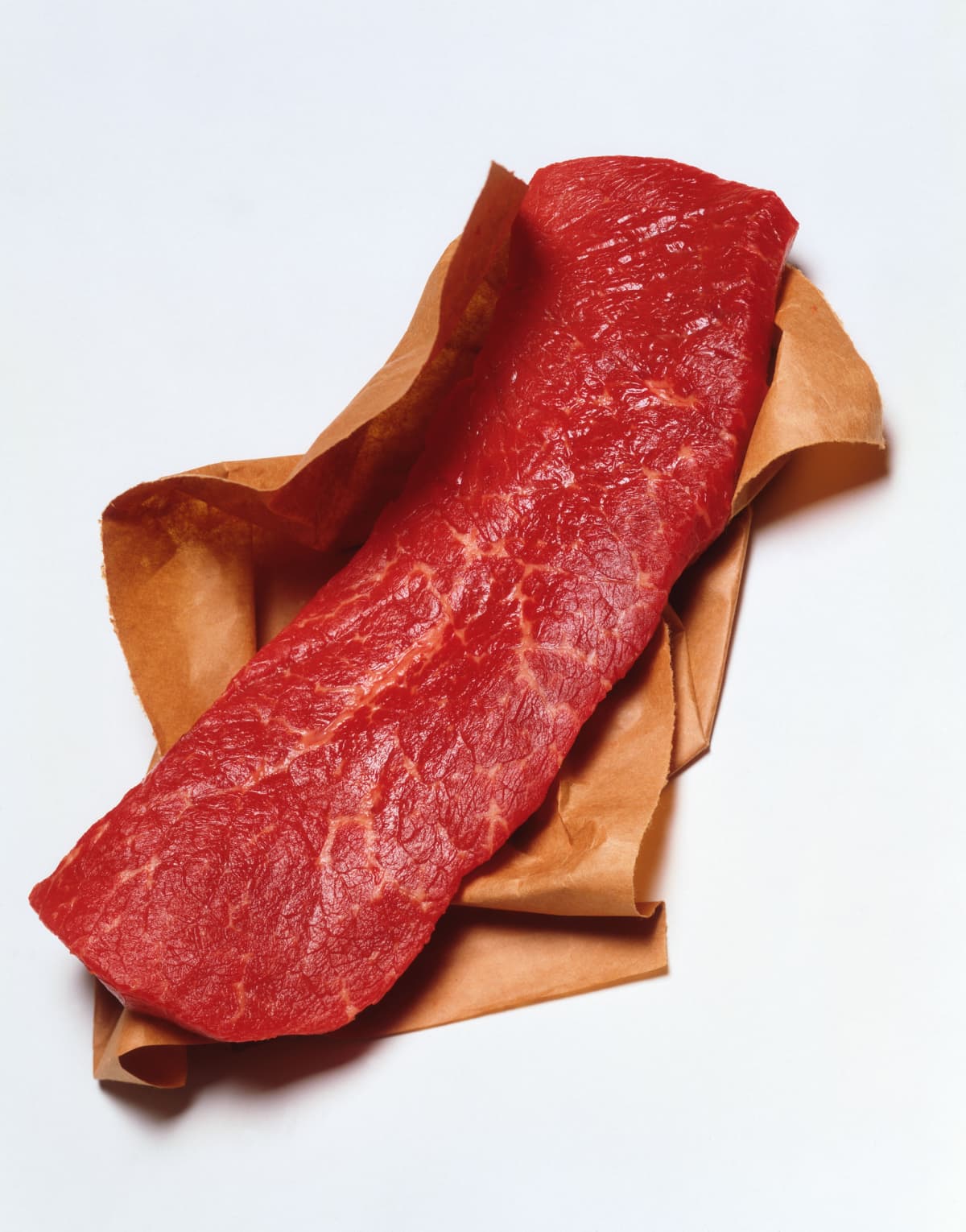 A slice of raw skirt steak on a white background.