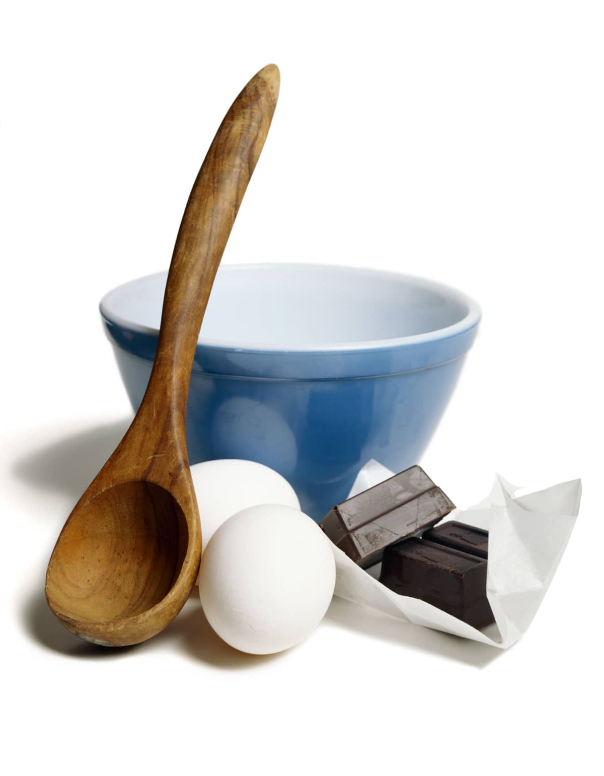 A blue mixing bowl with a spoon, eggs, and chocolate.