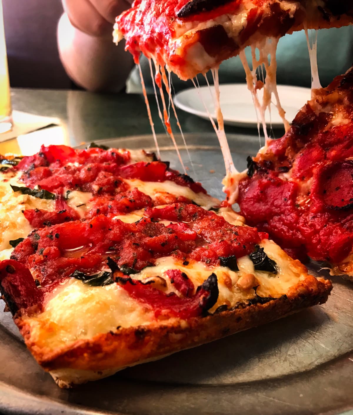 Detroit style deep dish pizza fresh out of the oven being served with gooey cheese and the caramelized crust edges.