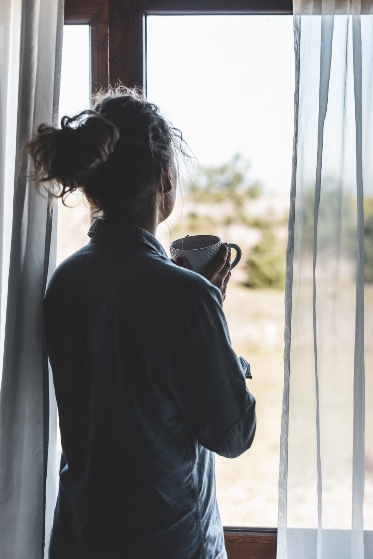 Silhouette of a woman drinking coffee next to the window