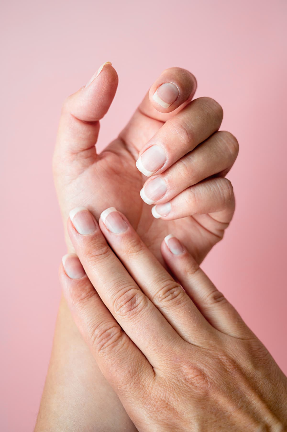 Female hand with natural healthy nails. Pink background.