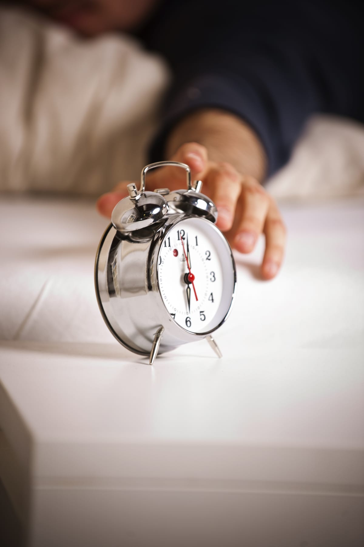 hand reaching out of bed to turn off alarm clock