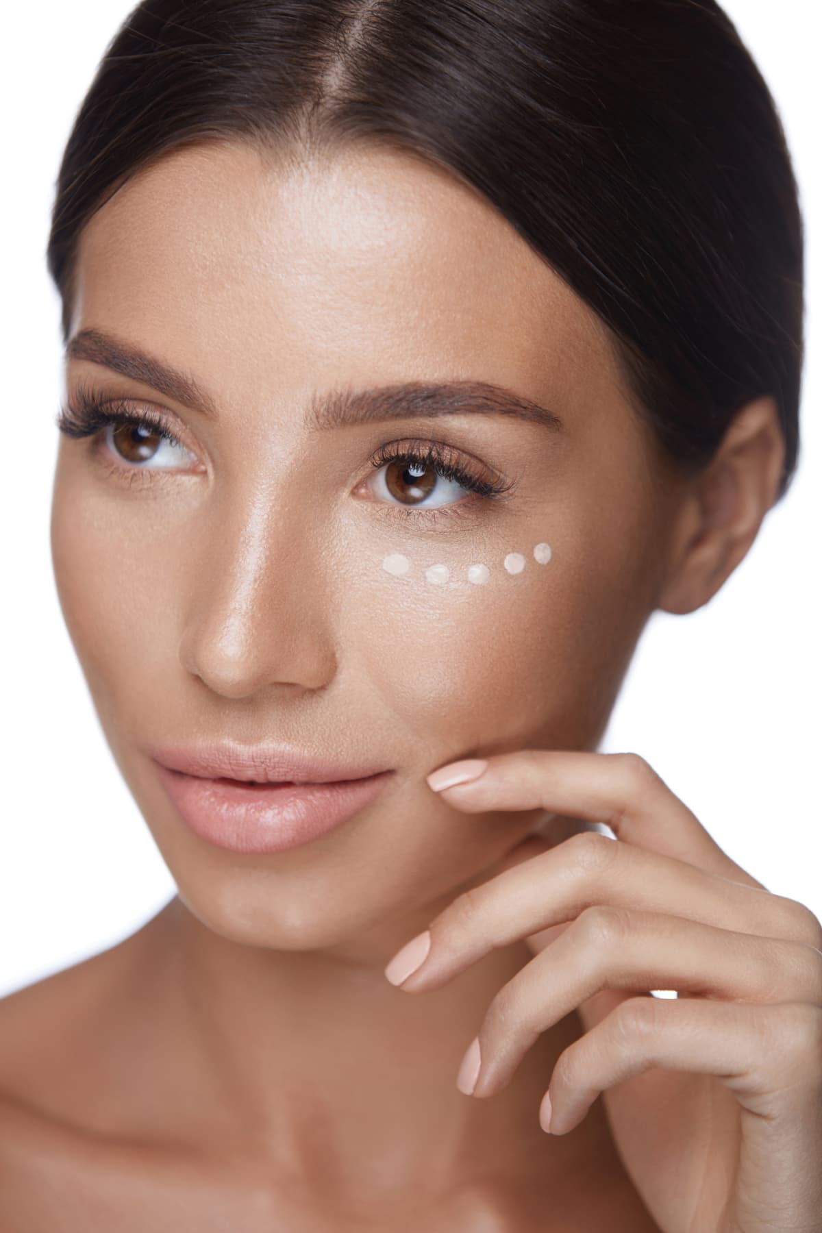 A woman dots concealer under her eyes