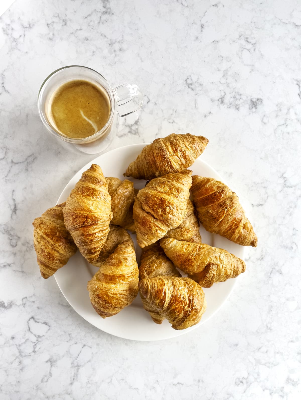 A cup of tea and a batch of croissants on a plate on top of a white marble counter.