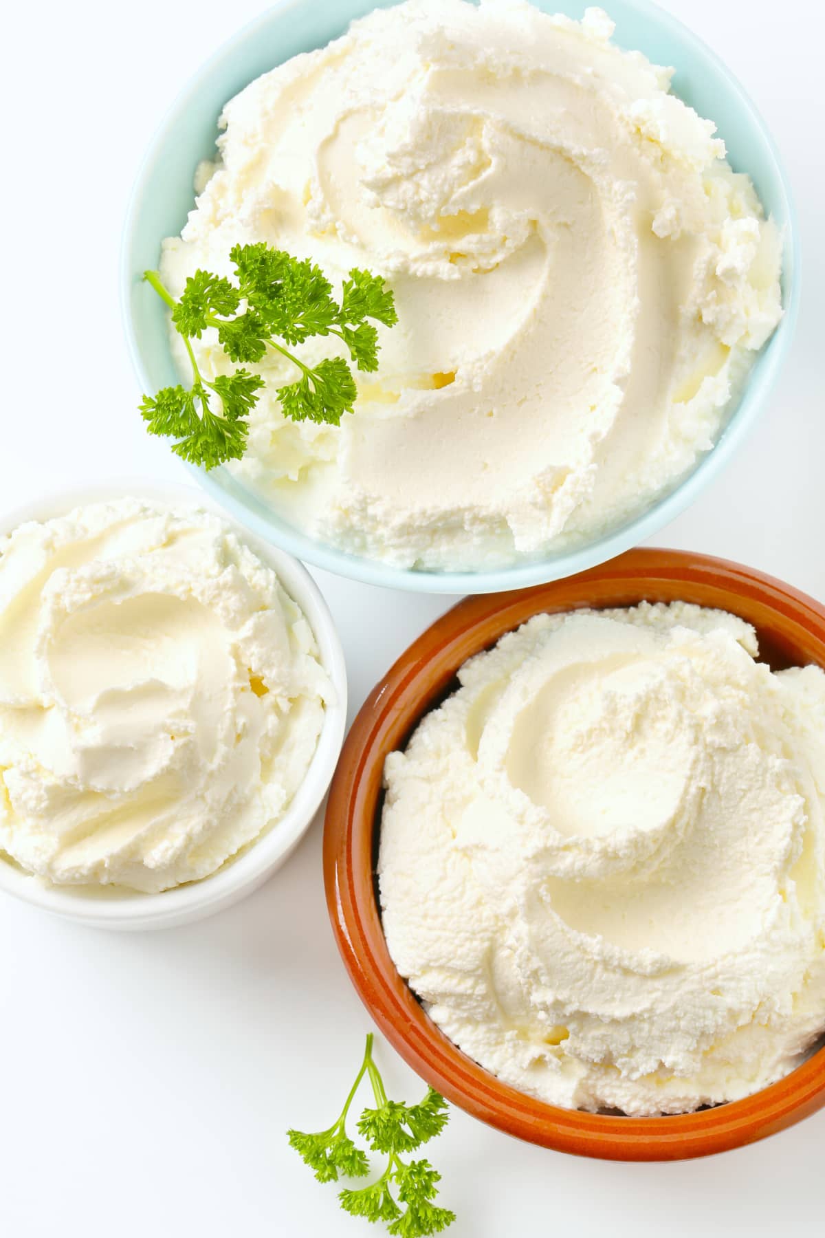 Cream cheese in various ceramic bowls on a white background