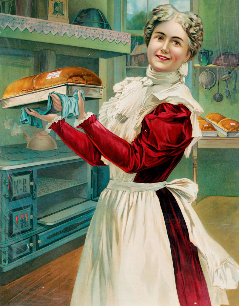Print shows a well-dressed woman wearing an apron, baking bread in a home-style kitchen; she is standing, three-quarter length, facing front, holding a pan of fresh baked bread in an advertisement for the J.A. Dahn & Son baking company. (Photo by: HUM Images/Universal Images Group via Getty Images)