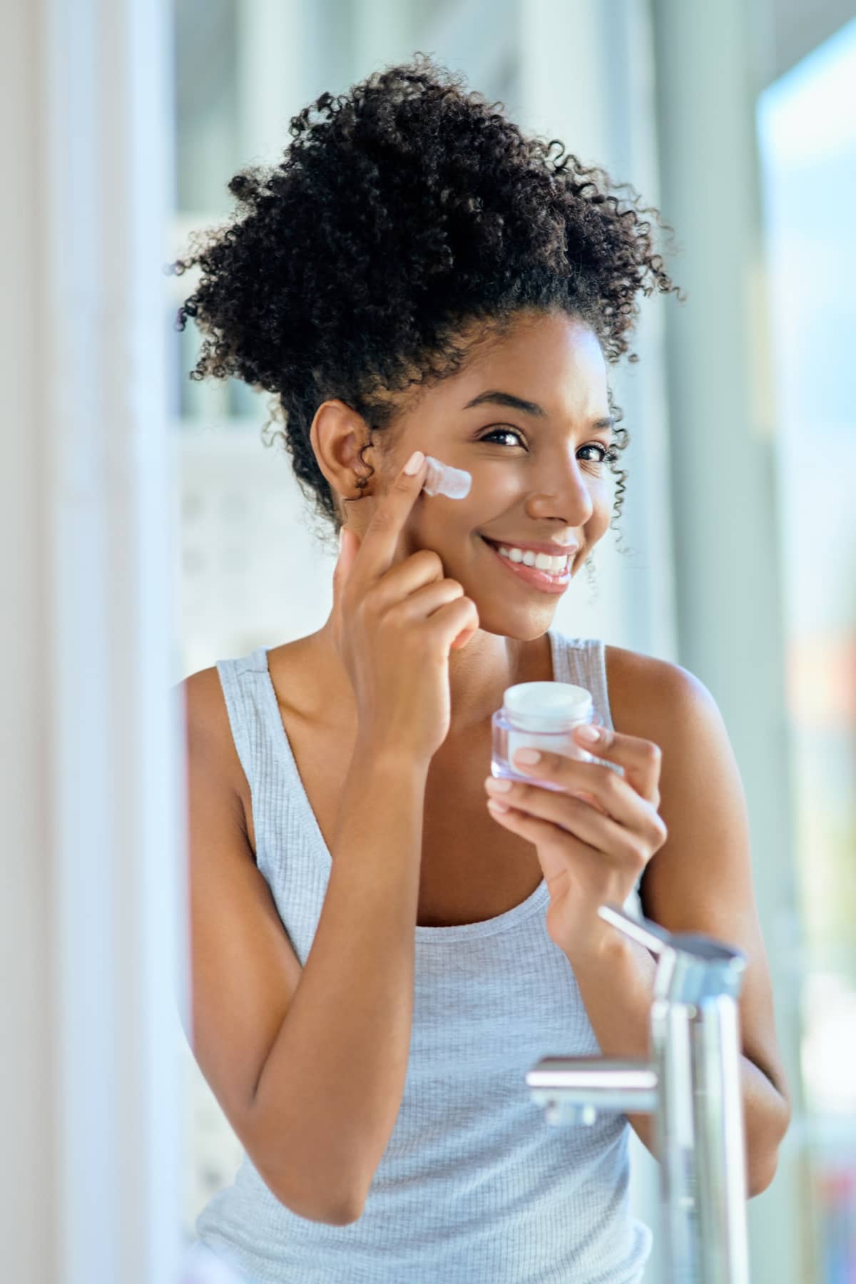  woman applying moisturizer to her face during her morning beauty routine.