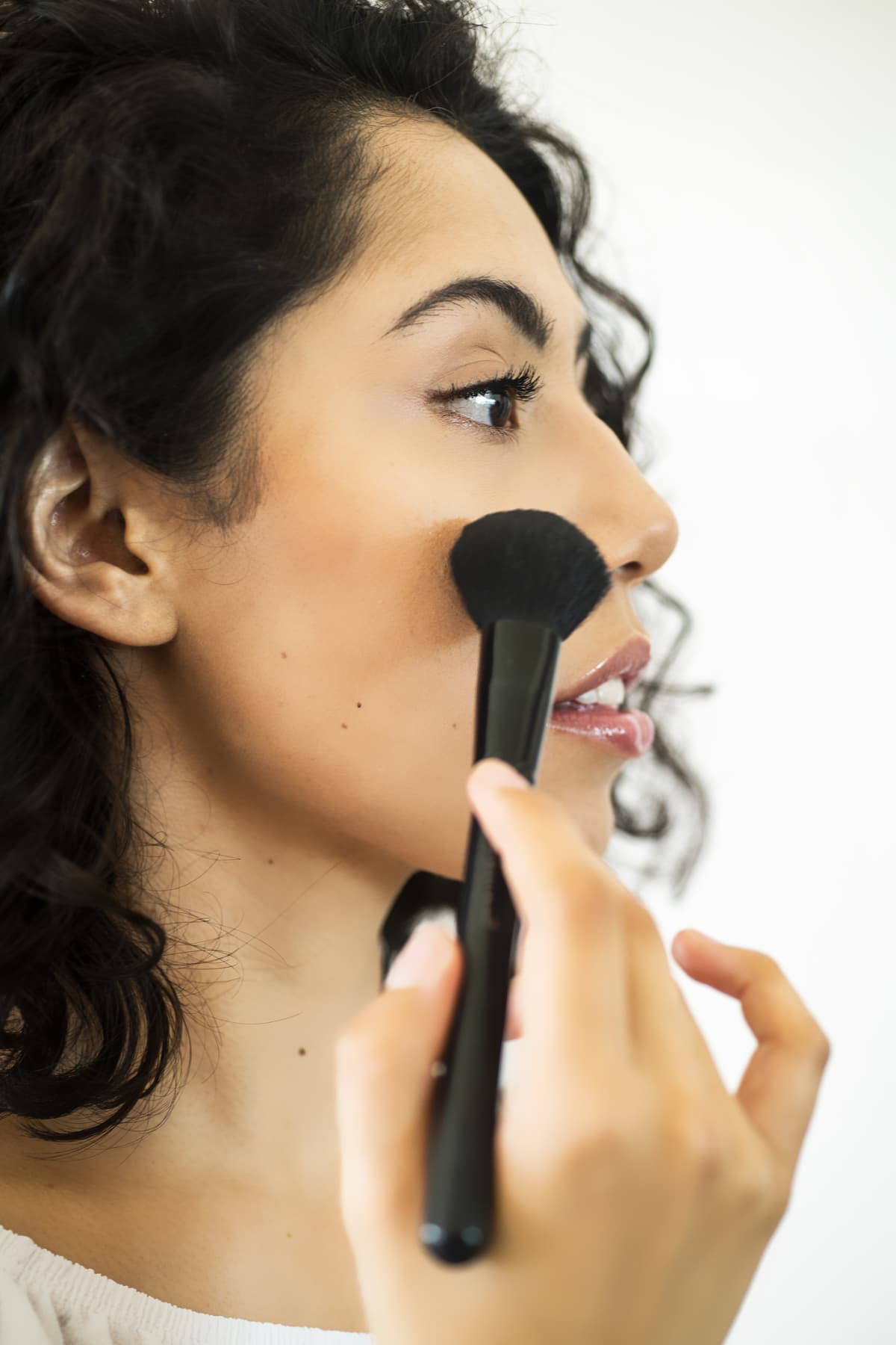 Latin young woman putting on makeup in front of the mirror