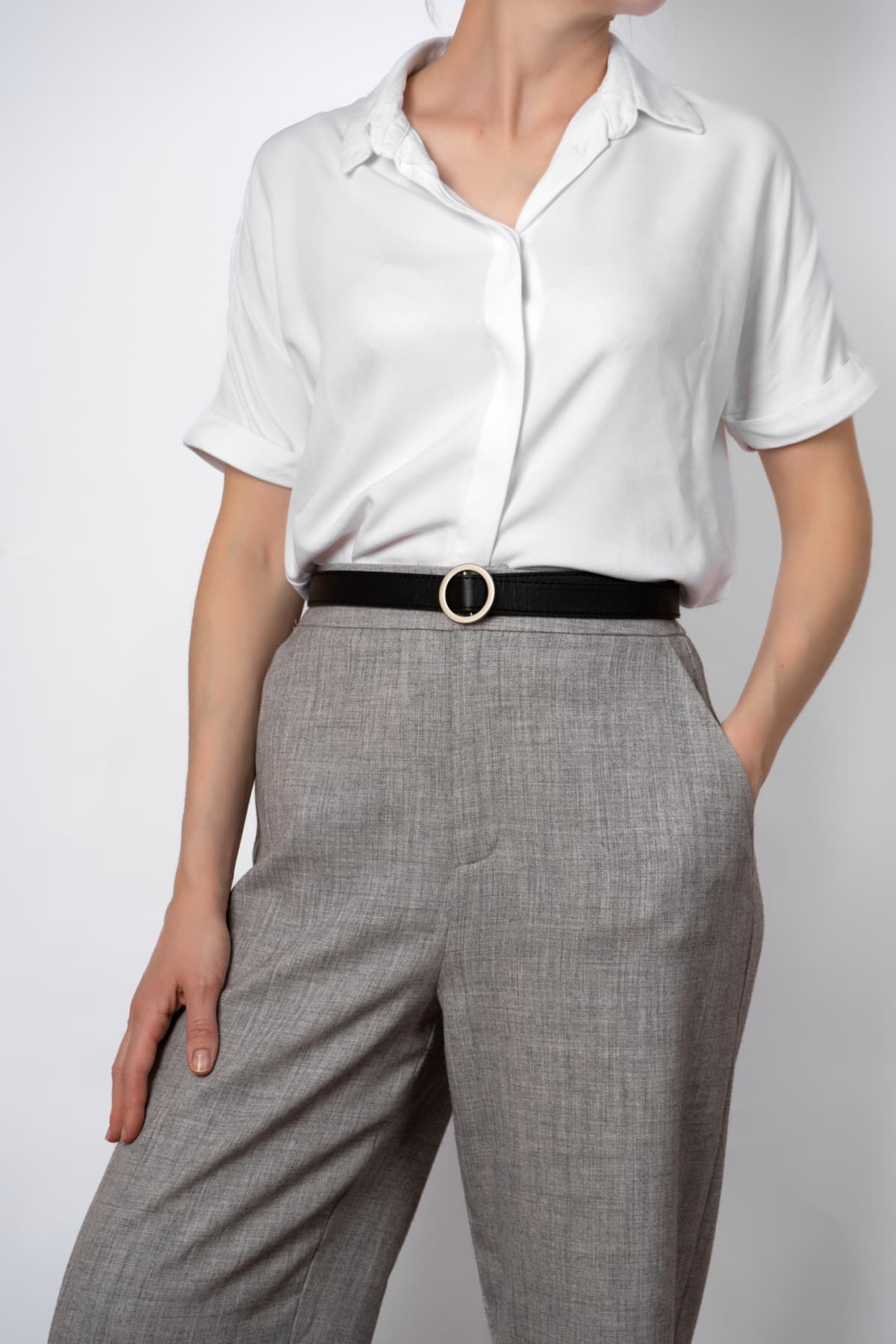 Fashionable women's casual spring outfit. woman posing in a white blouse and gray trousers. with black belt. close-up. faceless, hands in pocket, business style
