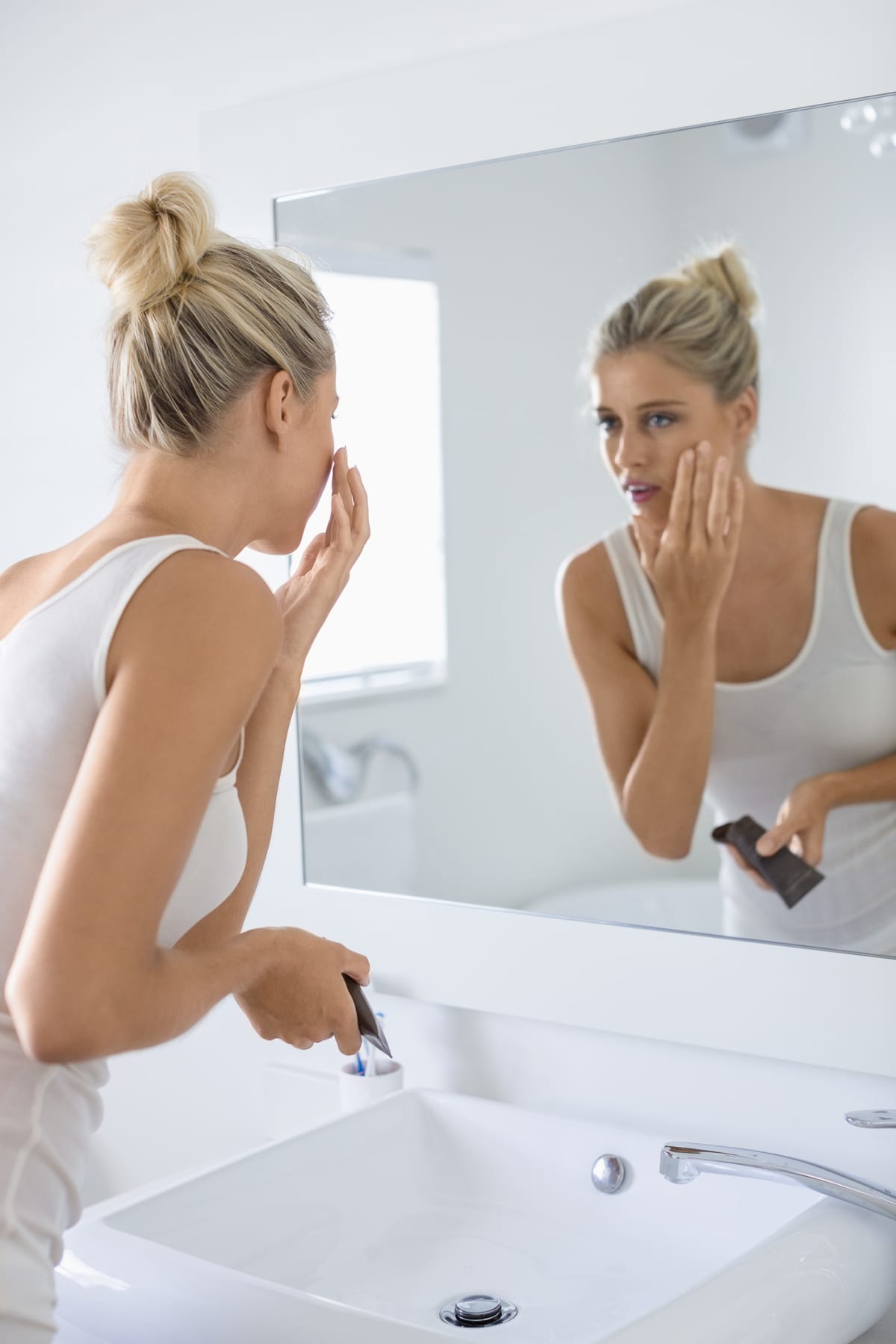 woman looking in mirror, applying cream on her face
