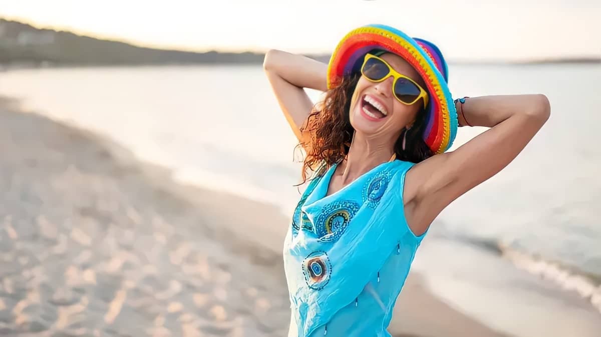 A happy woman wearing a colorful hat and yellow sunglasses.