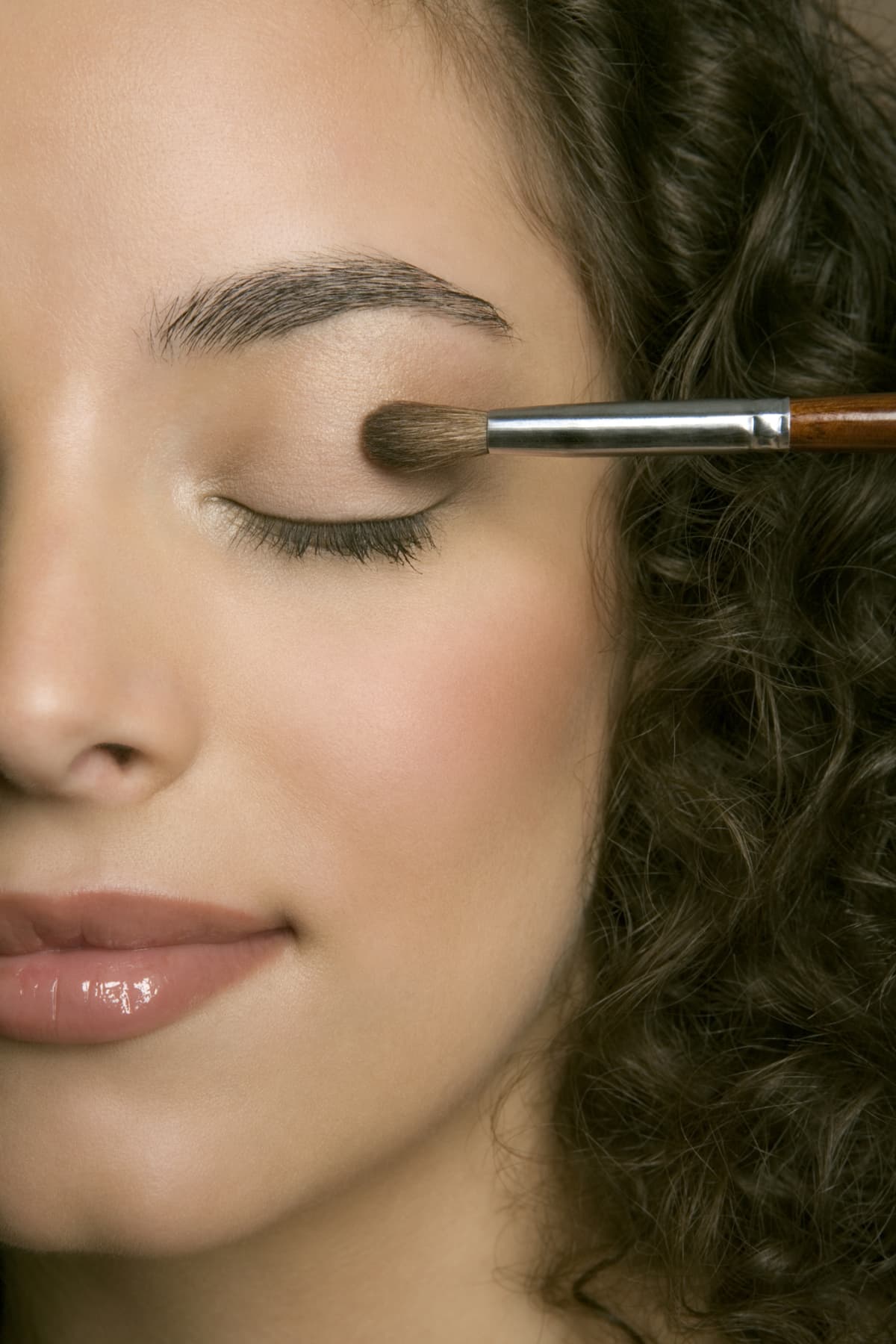 Young woman applying eyeshadow, eyes closed, close-up.