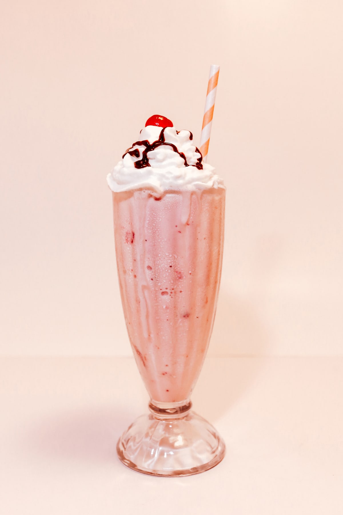 Strawberry milkshake containing strawberry ice cream. No people. 

Indulgence, unhealthy eating, sugar, sugary, dessert, retro image has copy space, room for text.