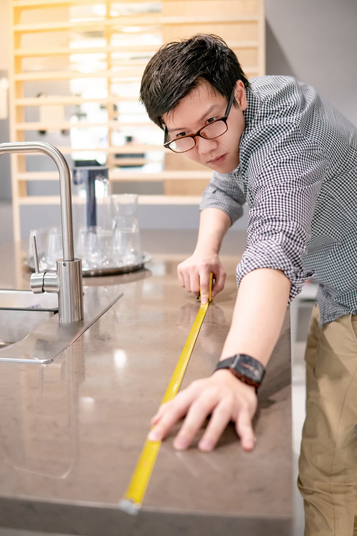Young Asian man utilizing a tape measure on granite countertops