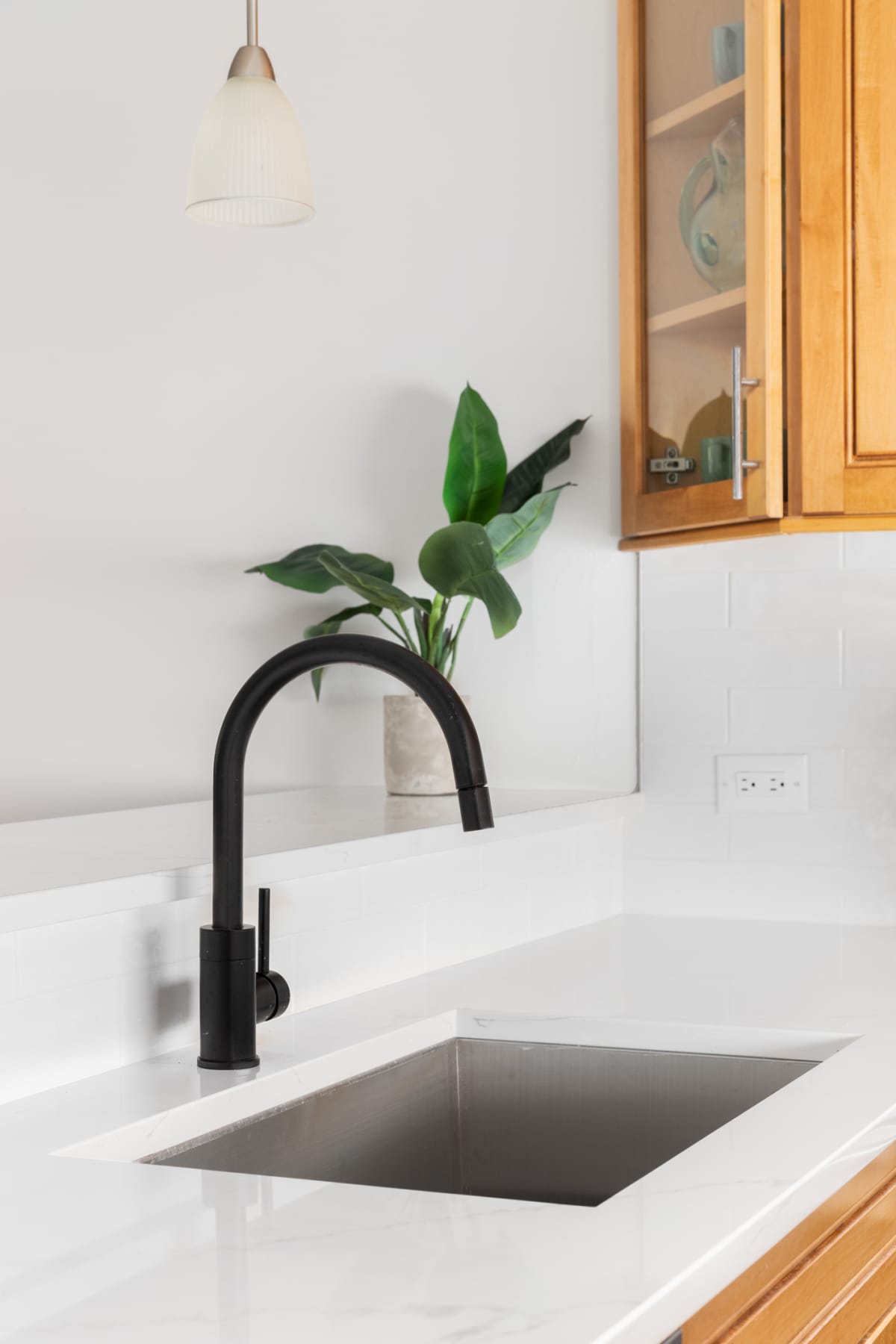 A kitchen sink detail shot with white marble countertop, black faucet, and a wood cabinets.