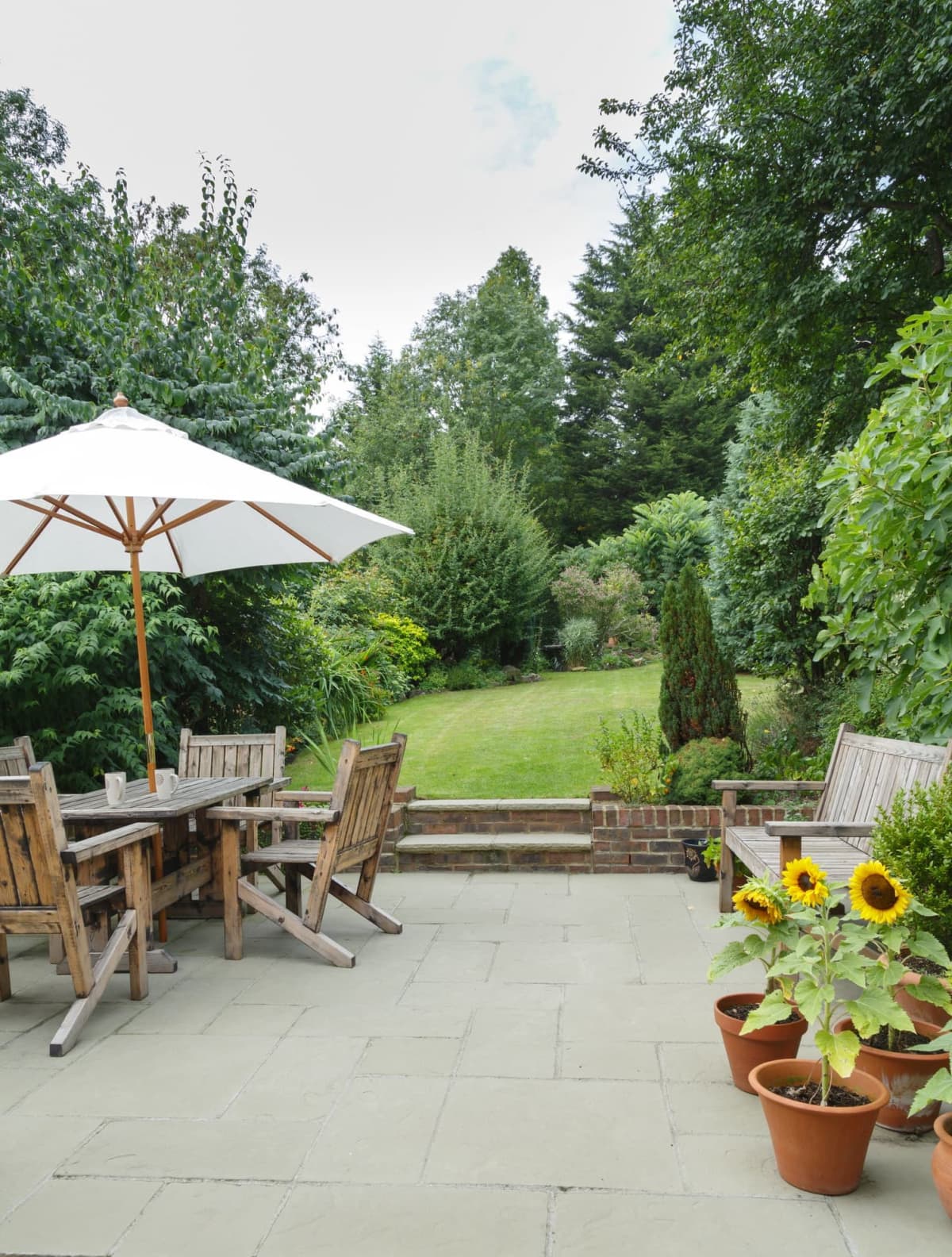 Garden in summer with patio, wooden garden furniture, and a parasol or sun umbrella