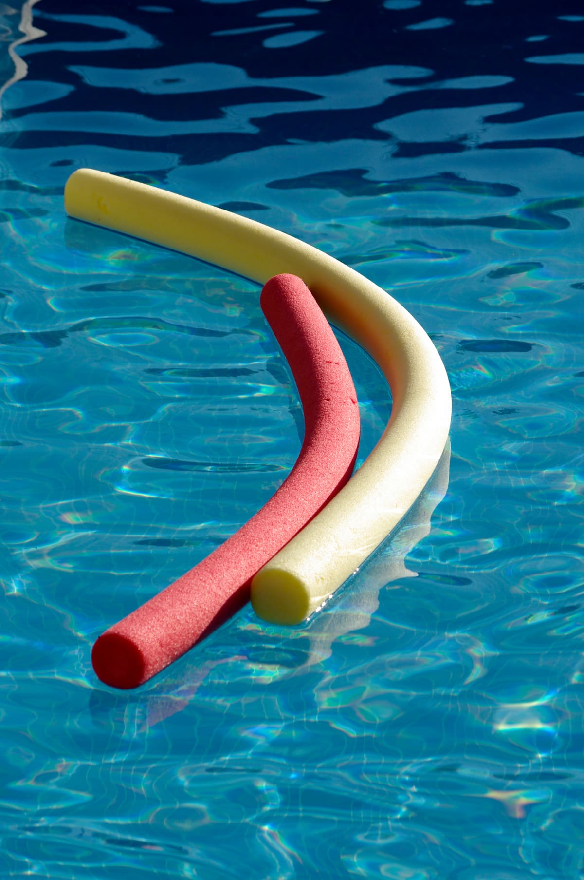 Yellow and red pool noodles (water logs) on pool in evening sunshine.
