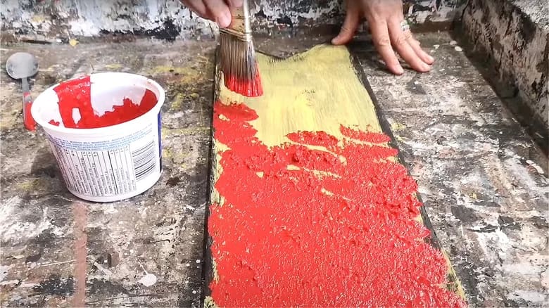 Person painting wood using paint brush and textured red paint