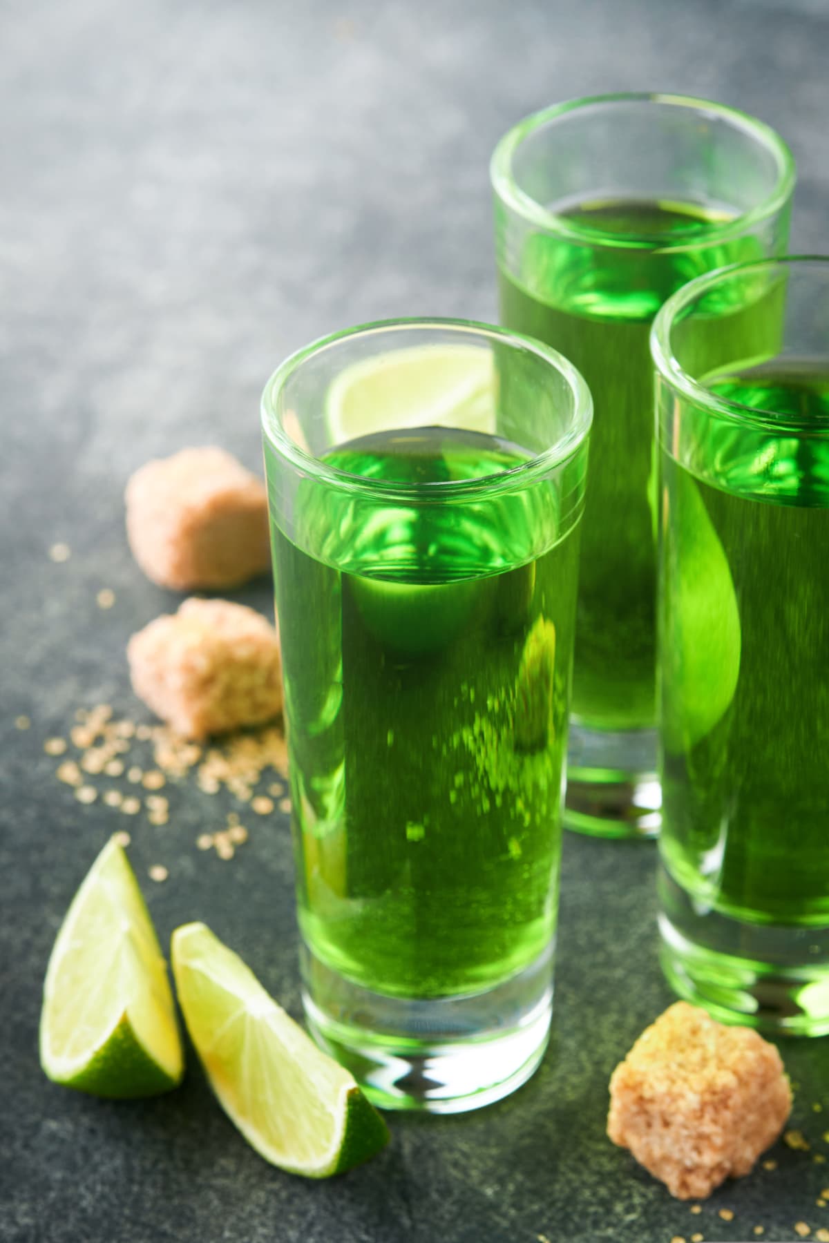 Two glasses of absinthe with cane sugar and lime on dark background