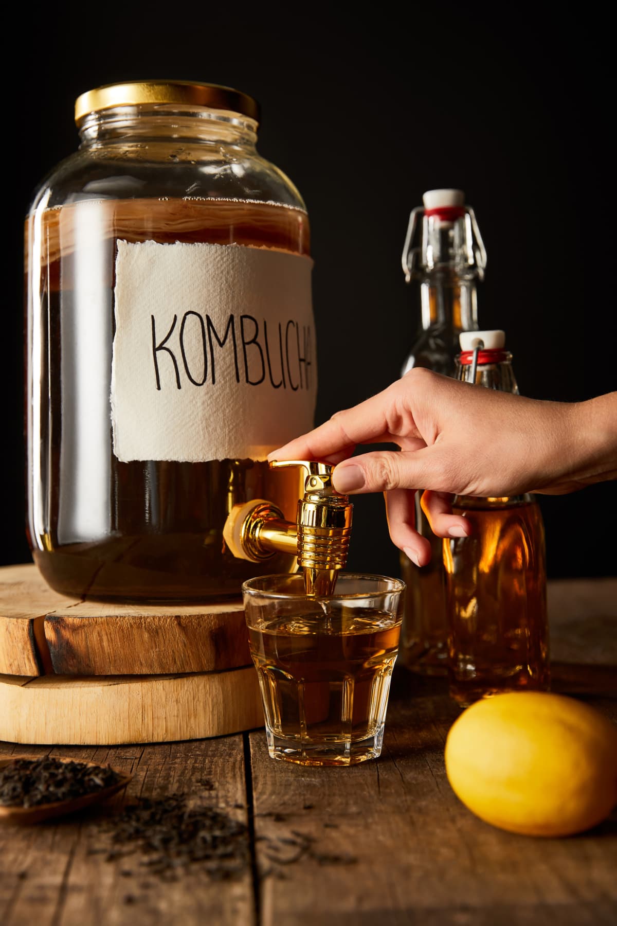 Kombucha being poured into a glass from a jar placed on a wooden surface