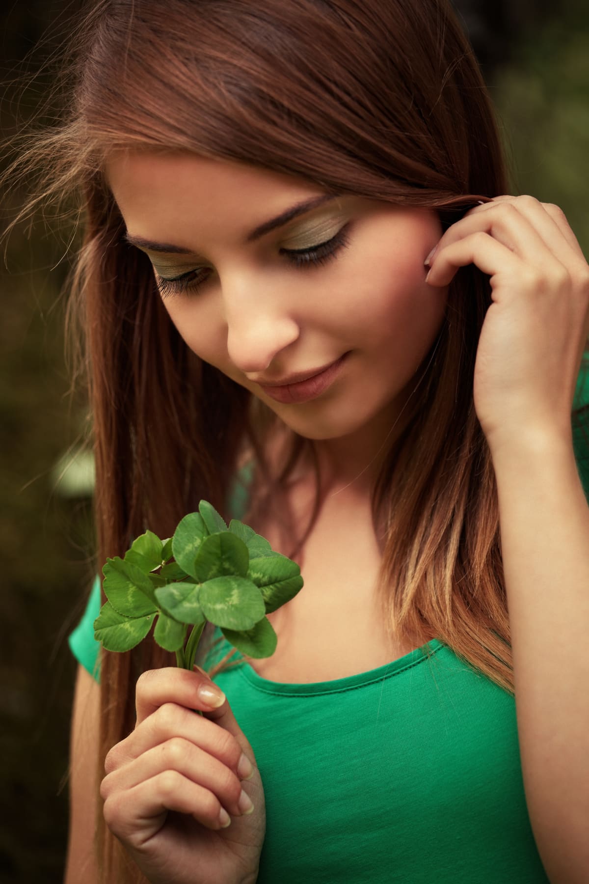 Young woman holds shamrocks as she tucks her hair behind her ear