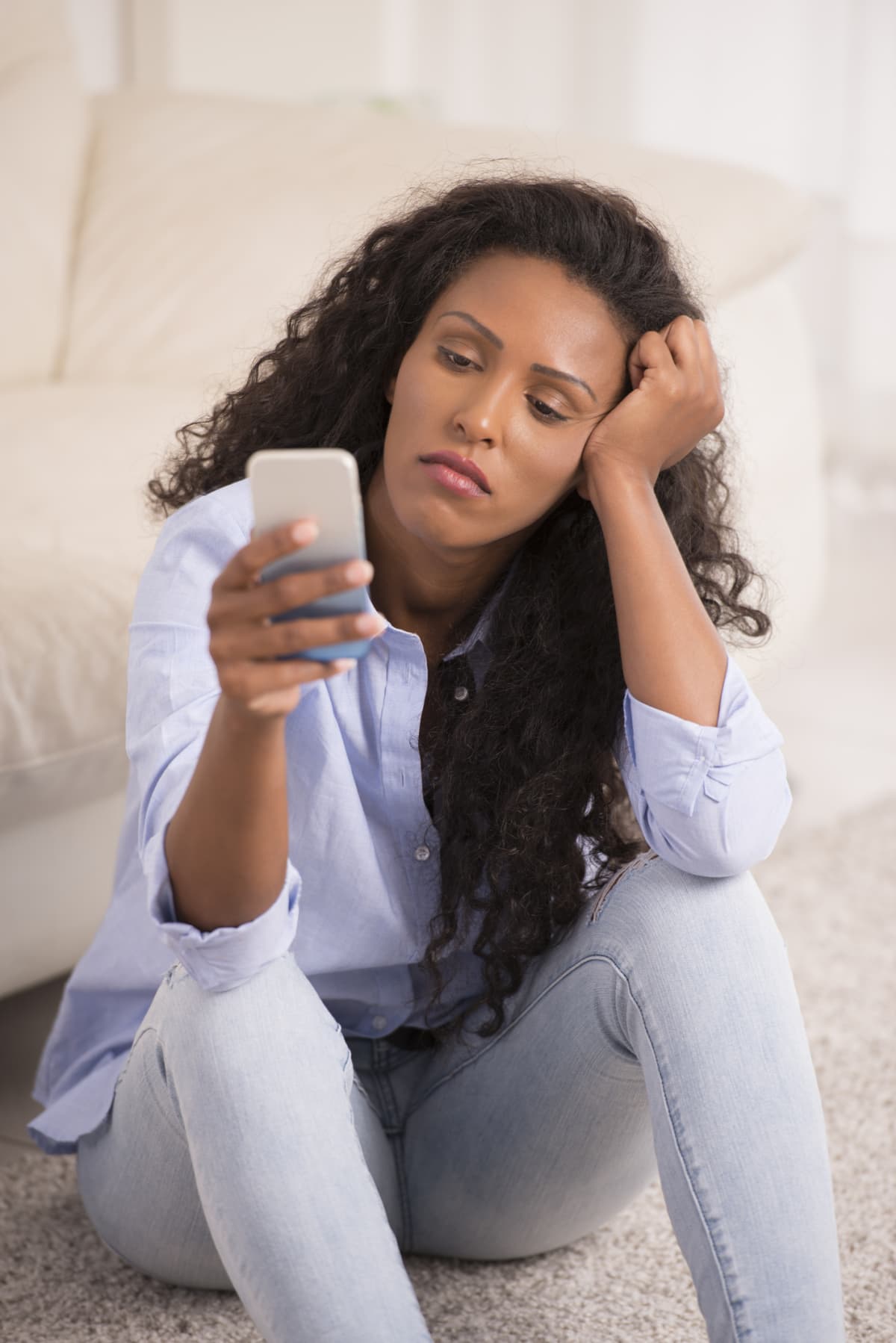 A woman looks forlorn while she stares at her smartphone screen.