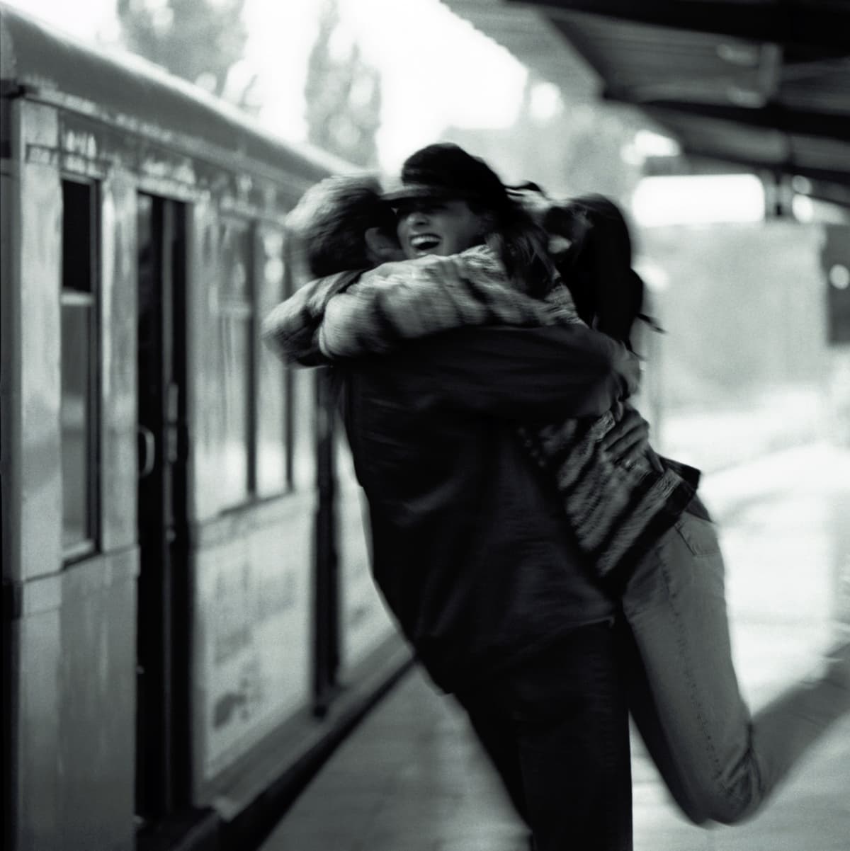 Couple embracing at train station, man lifting woman off the ground