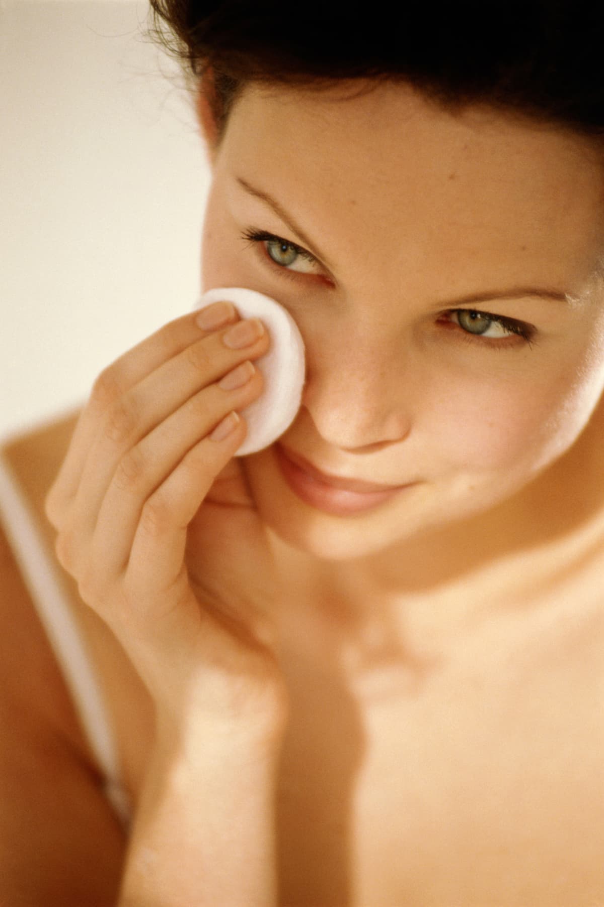 Young woman wiping face with cotton pad, close up