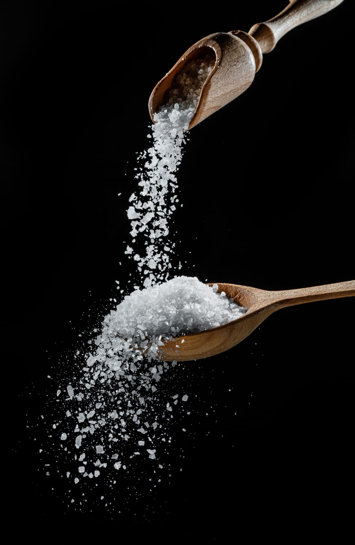 Edible salt crystals falling down into a wooden spoon against black background